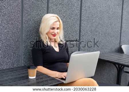 Young woman wearing smartwatch using laptop computer. Female working on laptop in an outdoor cafe.