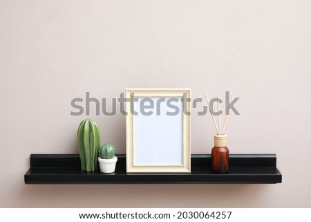 Empty photo frame, cactus figures and air reed freshener on shelf near pink wall