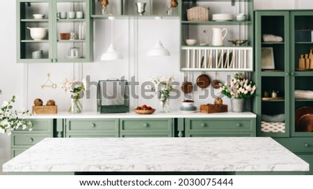 Clean and empty marble countertop, green vintage kitchen furniture with lots of flowers and bowl of strawberries, pair of white hanging pendant lights, various crockery in blurred background Royalty-Free Stock Photo #2030075444