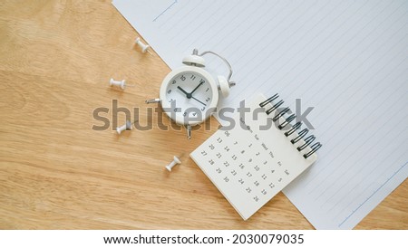 white calendar, thumbtack and analog alarm clock on school paper with line on wooden desk for back to school concept Royalty-Free Stock Photo #2030079035
