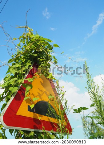 road sign of speed bump, covered by green vine