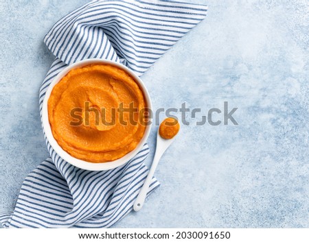 Pumpkin puree (mashed butternut squash) in white ceramic bowl top view. Blue and white stripes textile, white tea spoon. Copy space. Seasonal cooking concept. Ingredient for autumn baking. Royalty-Free Stock Photo #2030091650