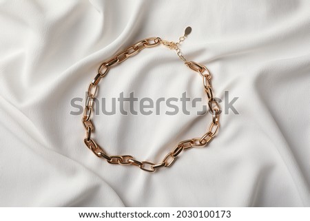 Elegant golden necklace on white fabric, top view. Stylish bijouterie Royalty-Free Stock Photo #2030100173