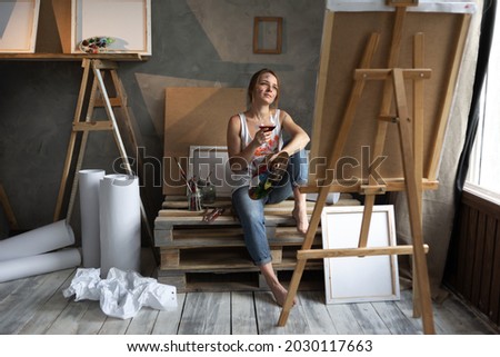 artist girl in a creative workshop thinking about looking for a muse for a picture while sitting with a glass of red wine. Creative people and alcohol addiction. Workshop or studio art. Mature Content