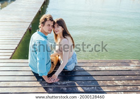 Couple of two, man and woman, sitting together on pier of wooden bridge in the sea or lake and hugging. Leisure, love relationships and people concept.
