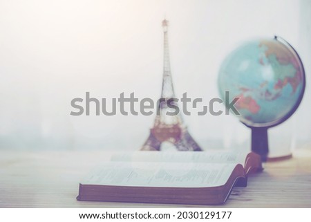 open bible with small world globe and small Eiffel tower on wooden table, window light. Christian background, bible study, or world mission ministry concept with copy space