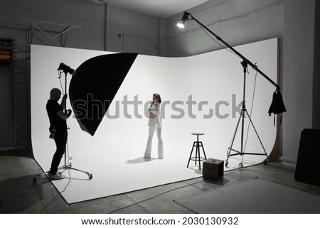 Fashion photography in a photo studio. Professional male photographer taking pictures of beautiful woman model on camera, backstage