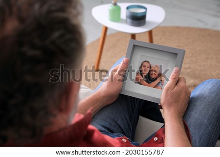 Senior man holding frame with photo of his wife and granddaughter at home, closeup