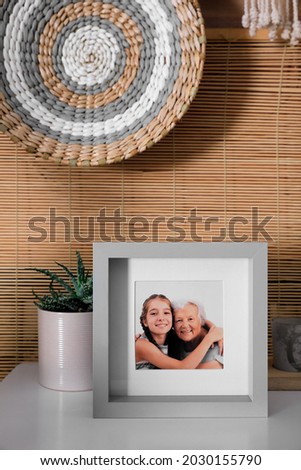 Frame with photo of elderly woman and her granddaughter on white table indoors