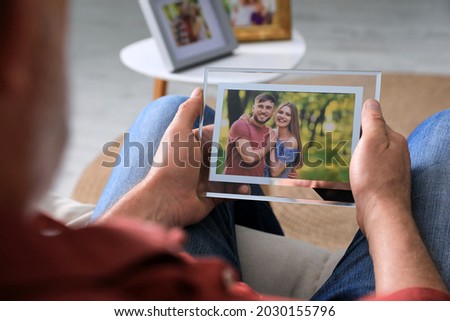 Senior man holding frame with photo of young couple at home, closeup