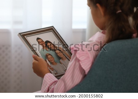 Little girl holding framed family photo indoors, closeup
