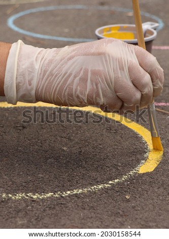 a hand with paintbrush drowing a circle with a yellow paint on asphalt