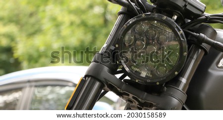moto headlight close-up and a car in the background