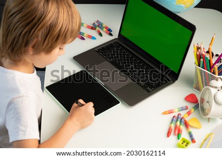 little boy with laptop and graphics tablet, green chromakey on laptop.