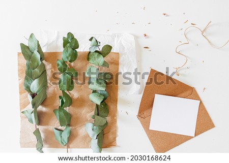 Creative retro style composition of craft envelopes, blank paper sheet and eucalyptus branches on white background. Florist, flower shop, gift concept.