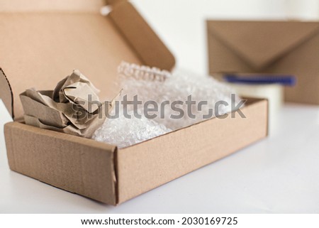 Corton box with packaging paper and bubble wrap inside. Envelope and tape in the background. Royalty-Free Stock Photo #2030169725