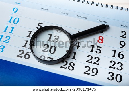 The magnifying glass lies on a blue calendar with certain date. Planning business, important meetings and events. Research and analysis concept. Create reminders. Closeup top view. Royalty-Free Stock Photo #2030171495