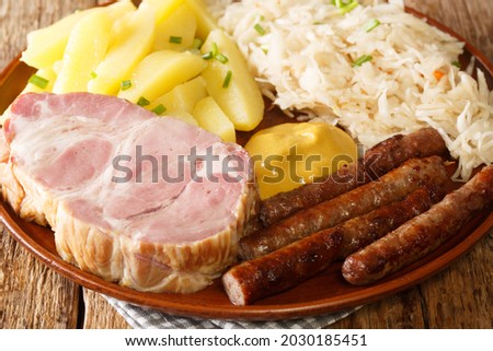 German Kassler pork neck with Sauerkraut potatoes and mustard on wooden table closeup in the plate on the table. Horizontal
