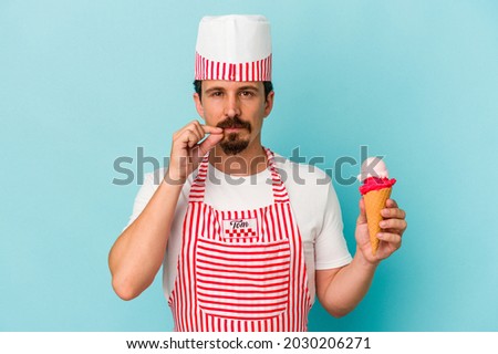 Young caucasian ice cream maker holding a ice cream isolated on blue background with fingers on lips keeping a secret.