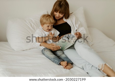 Mom baby sitter and cute little kid son read book fairy tale in bed, cute small child boy listening to mom learn reading in bedroom in morning. Happy little boy listen and smiling