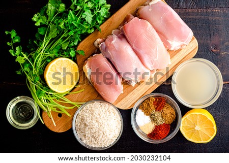 One Pan Spanish Chicken and Rice Ingredients: Raw chicken thighs, rice, spices, and other ingredients on a wood table