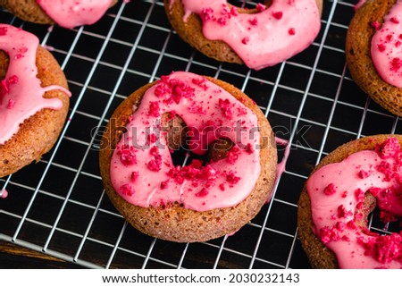 Raspberry Baked Donuts with Raspberry Glaze on a Wire Cooling Rack: Baked donuts with pink raspberry glaze and red sprinkles