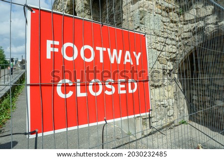 Footway closed warning sign tied to metal fencing. Historic walls in background 