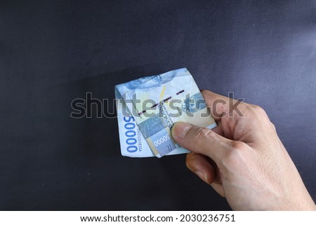 Male hand showing Indonesian rupiah note. Indonesian Rupiah the official currency of Indonesia. Business concept, Black Background.
Male hand making payment.
Uang 50000 Rupiah Indonesia