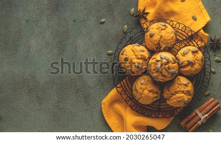 Pumpkin muffins with spices and pumpkin seeds on metal cooling rack top view. Copy space. Dark green background. Autumn, halloween, thanksgiving baking concept. Rustic table, orange textile.
