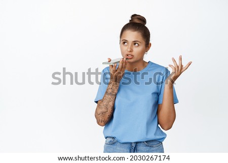 Young woman record voice message, using voice translator app on smartphone, standing against white background