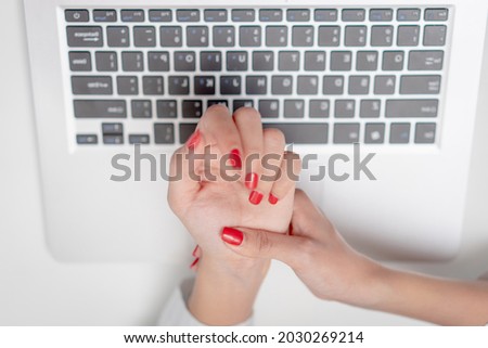 Close up hands of young woman with red nails using a laptop suffering from carpal tunnel syndrome.