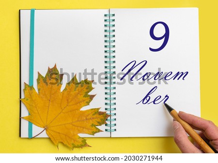 9th day of november. Hand writing the date 9 november in an open notebook with a beautiful natural maple leaf on a yellow background. Autumn month, day of the year concept.