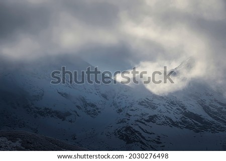 Dramatic cloudscape in Tatra Mountains, Poland. Sunlight behind the peaks illuminating the clouds and fog covering the trail to Świnica Peak. Selective focus on the ridge, blurred background.