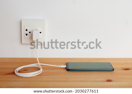 Plug in power outlet Adapter cord charger of smart phone on wooden floor Royalty-Free Stock Photo #2030277611