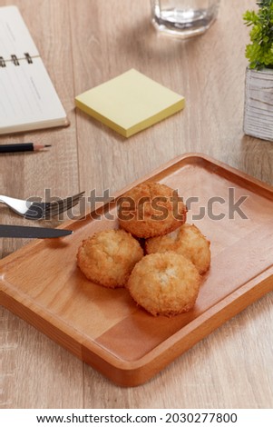 Real shoot. Work and eat with coconuts cake. Coconuts cake on wooden plate in wooden table. Around the croissant are glass of water, take note, pencil, sticky notes. Clean, modern conce