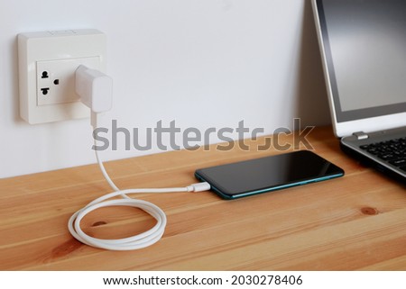 Plug in power outlet Adapter cord charger of smart phone on wooden floor Royalty-Free Stock Photo #2030278406
