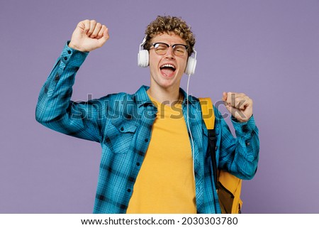 Young fun boy teen student in casual clothes backpack headphones glasses listen to music isolated on plain pastel light violet background studio. Education in high school university college concept