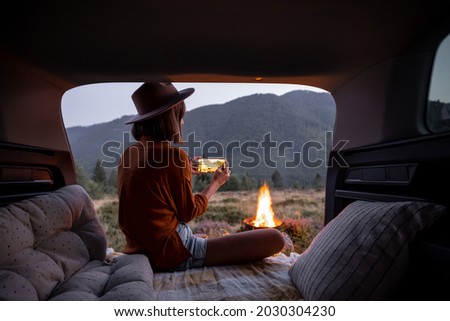 Woman photographing a bonfire on phone, traveling by car in the mountains at dusk. Camping and vacation in the mountains alone, travel by car concept Royalty-Free Stock Photo #2030304230
