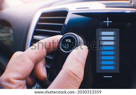 Car owner hand turning volume button of a car audio system in the car Royalty-Free Stock Photo #2030313359