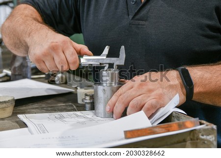 The worker measures the part with a vernier caliper and checks the size against the drawing.