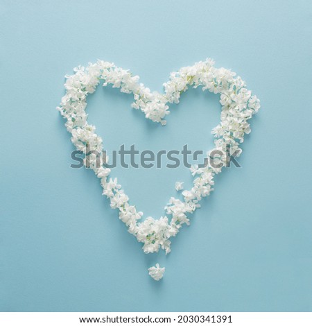 Heart frame made of fresh white flowers on light blue background. Copy space.