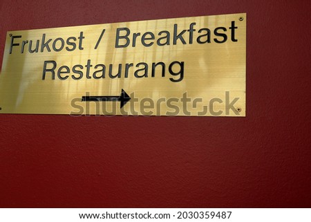 Golden sign for breakfast at a Swedish restaurant. Arrow points the way. Red background. Close up and isolated. Västergötland, Sweden.
