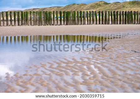 View on wooden poles at white sandy North sea beach near Zoutelande, Zeeland, Netherlands during low tide, reflection in water