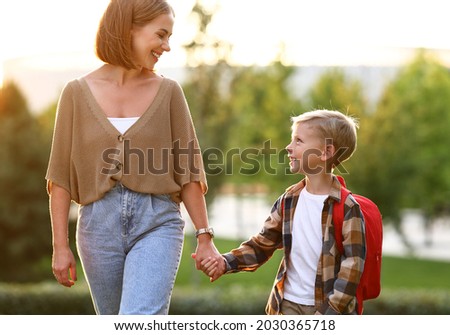 Mother and little son schoolboy with backpack holding hands, going to school together through park on sunny autumn day, cute happy boy looking at mom with smile and being ready to study Royalty-Free Stock Photo #2030365718