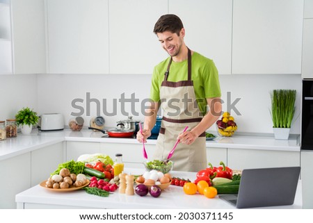 Photo portrait young man in apron cooking vegetables salad with laptop