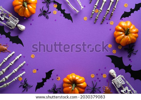 Halloween decorations on violet background. Flat lay pumpkins, bats, spiders, skeletons and confetti. Top view with copy space. Halloween concept.