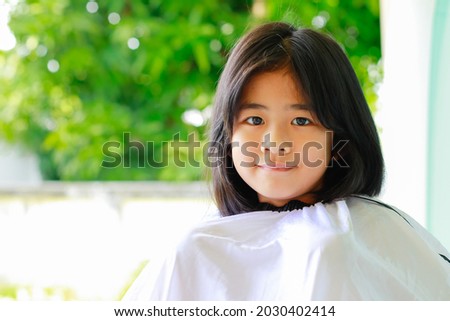 Happy little girl in a veil to cut her hair at home in new normal concept.