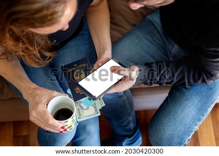 Man and woman using a mobile phone with dollars, passport, credit cards and coffee in hand