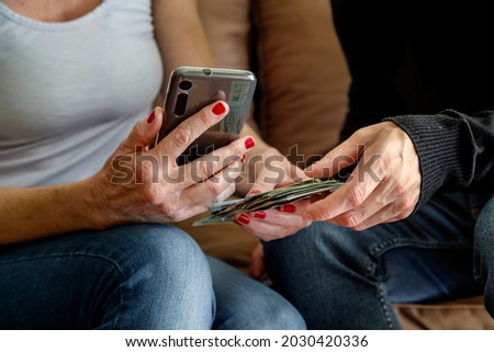Man and woman consult their smartphone with dollars and credit cards in hand