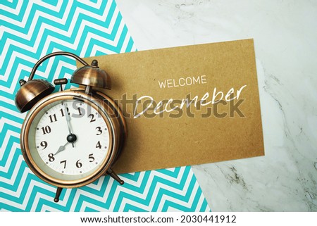 Welcome December typography text on paper card with alarm clock on marble background